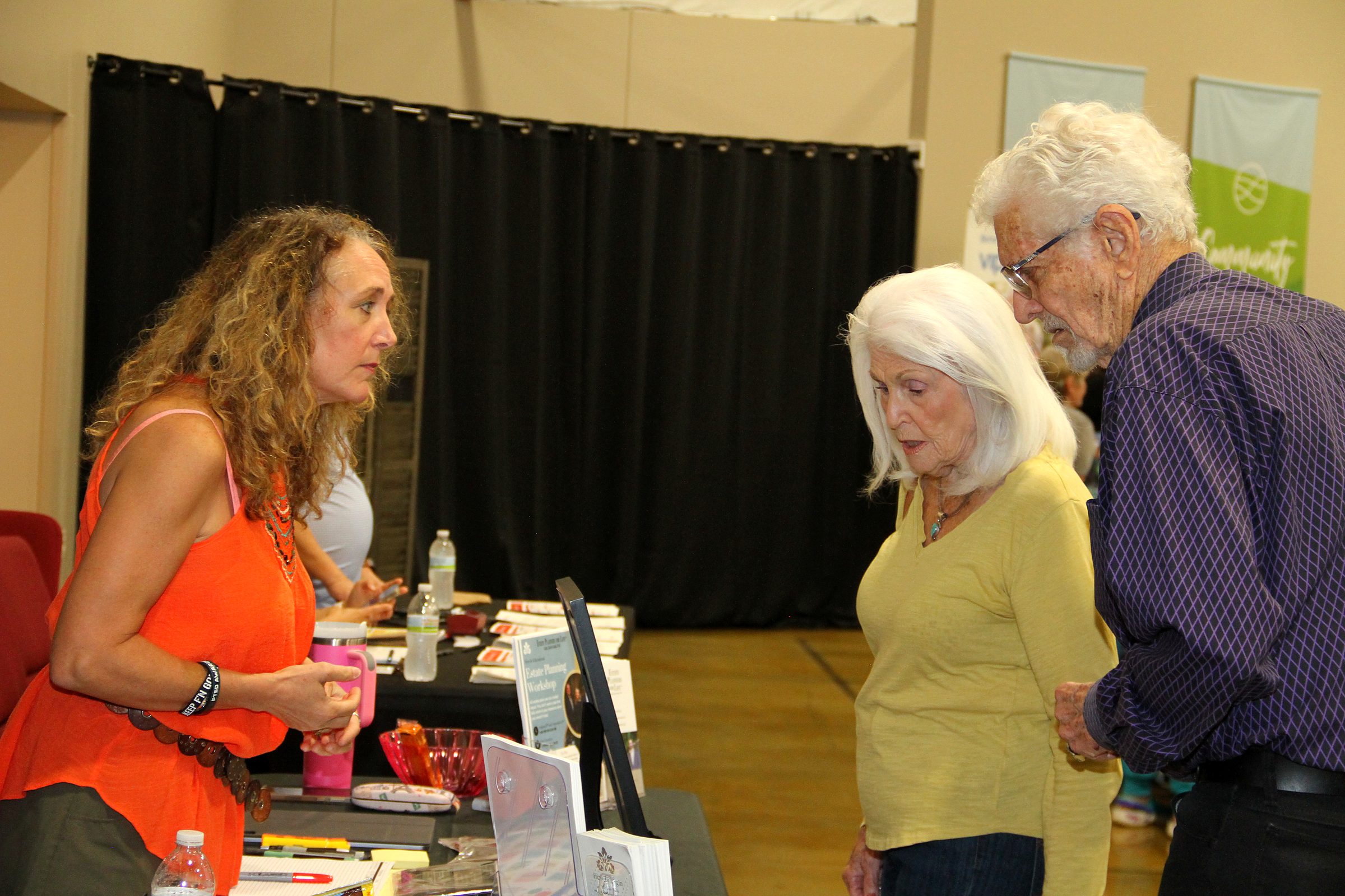 A member of the team talking with a couple at the firm's booth at a community senior expo