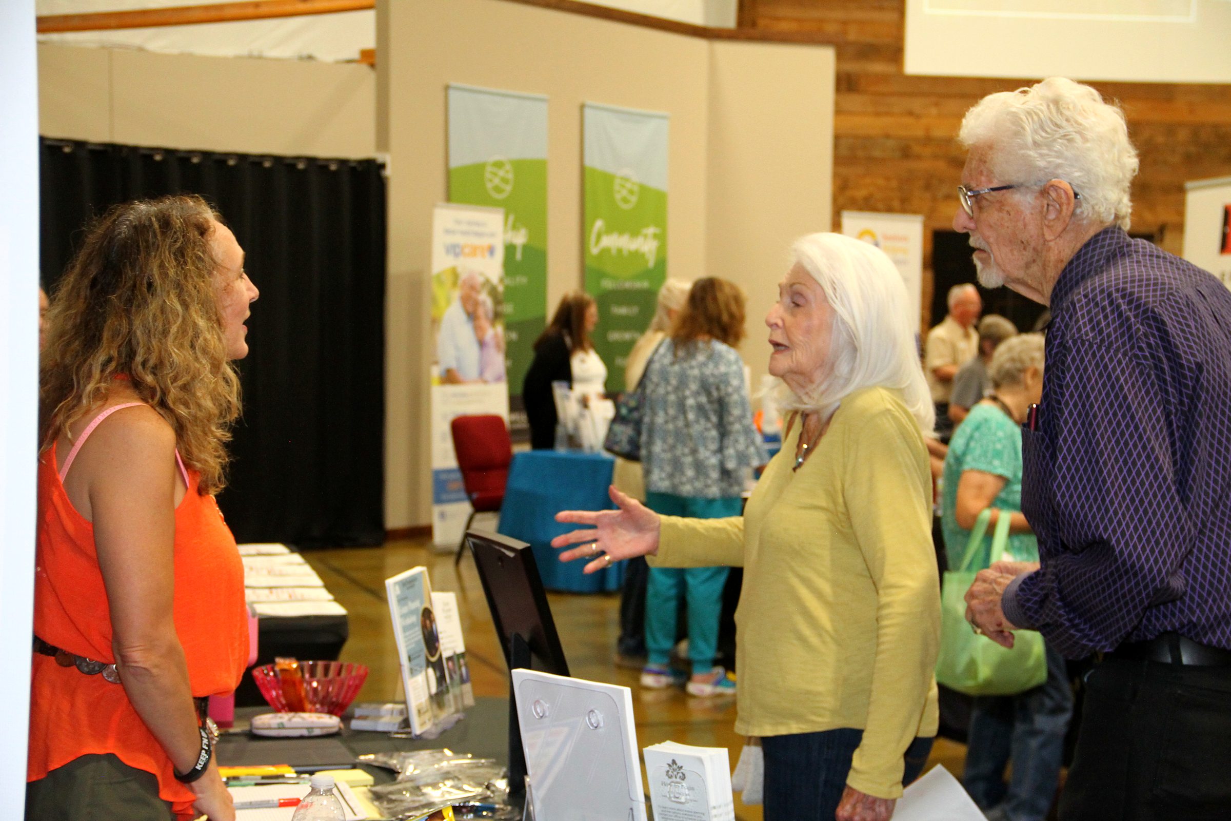 A member of the team in conversation with visitors, the expo hall behind, at a community senior expo