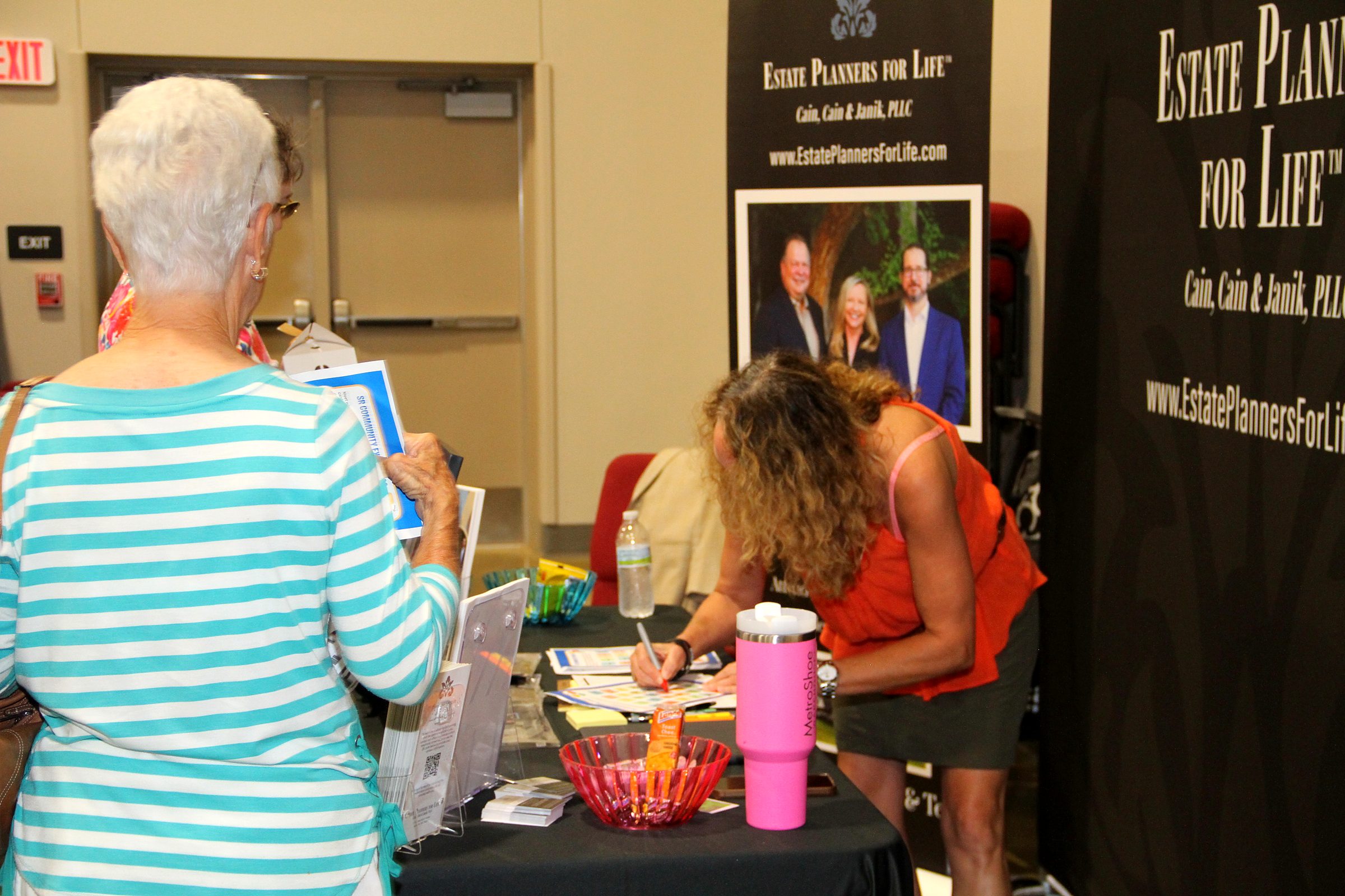 Visitors at the firm's booth, one of them signing up, at a community senior expo