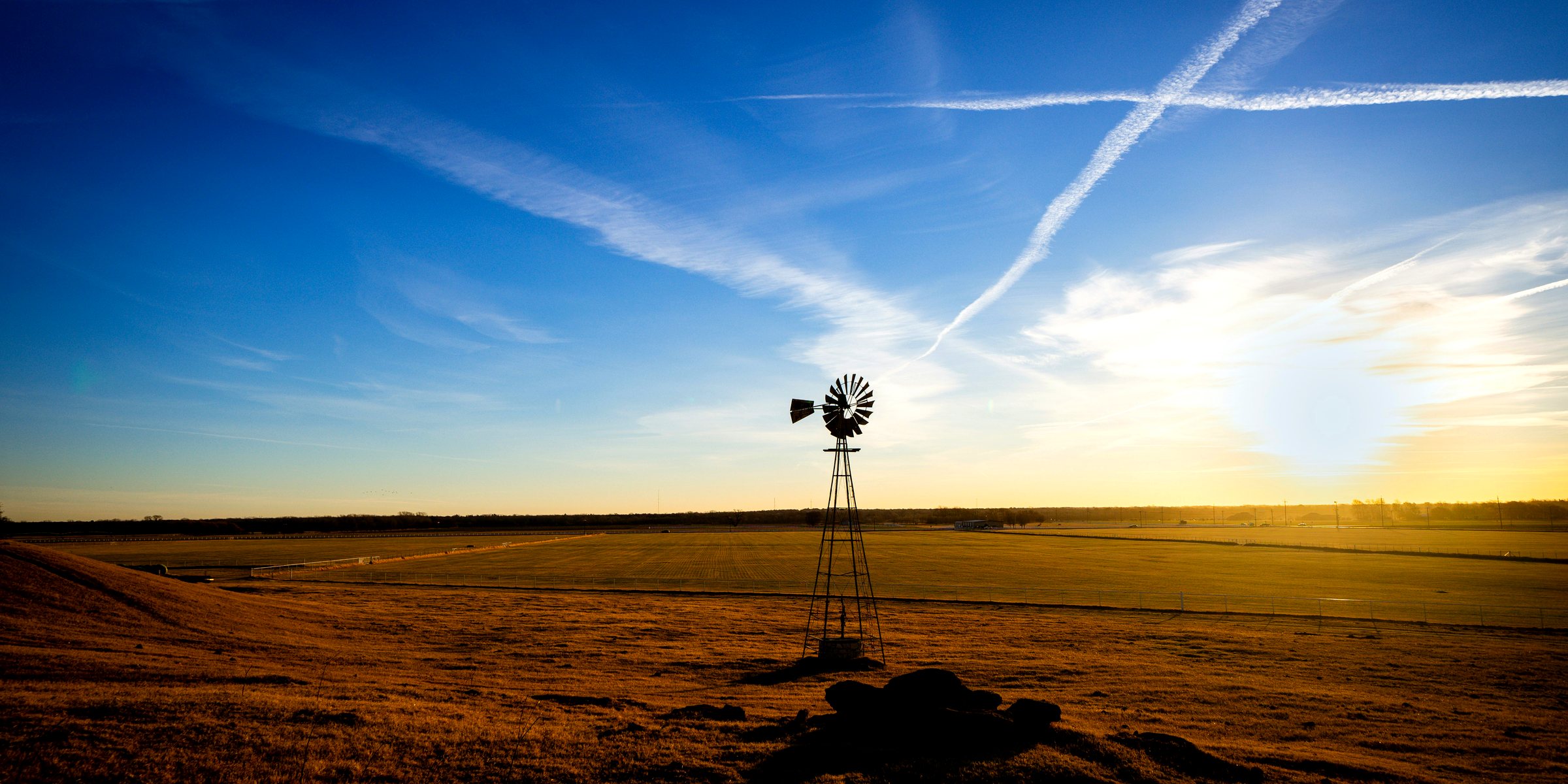 A windmill standing over open prairie at sunset