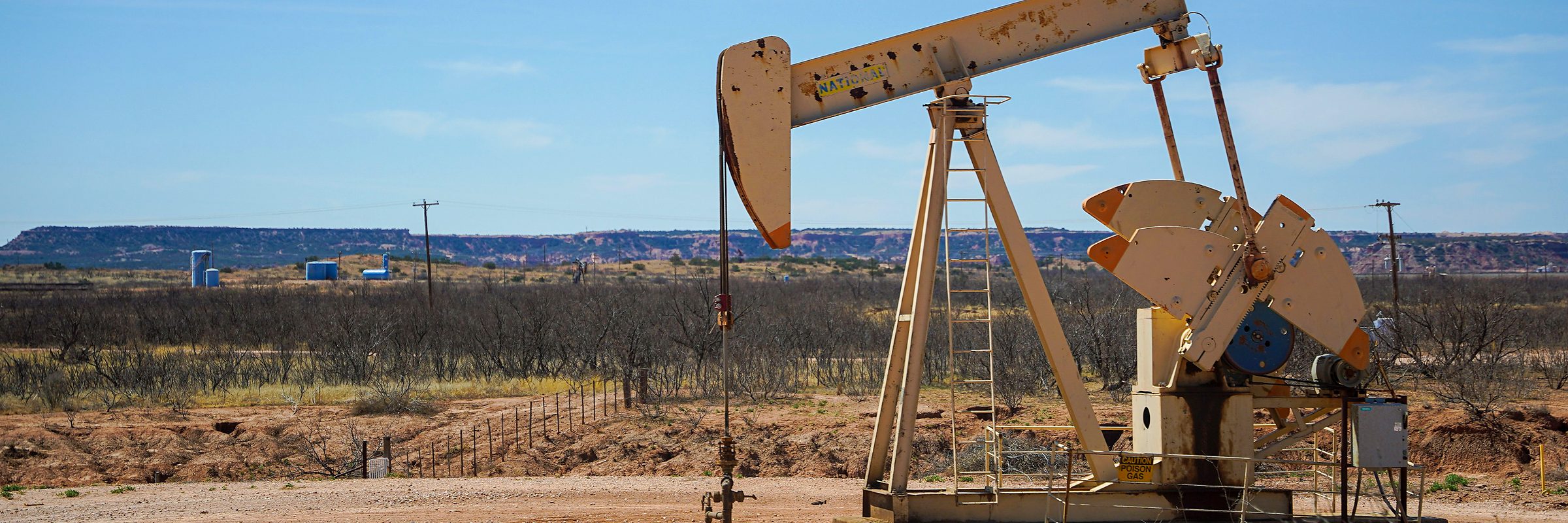 A pump jack working on red dirt under a wide sky
