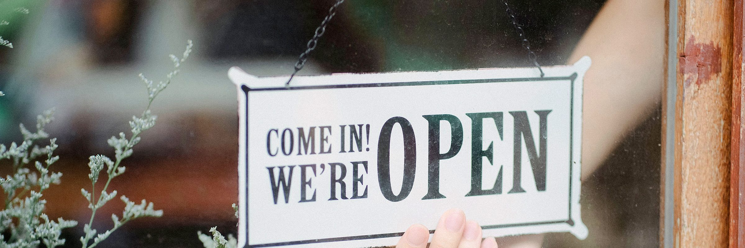 A hand turning the open sign on a shop window at the start of the day
