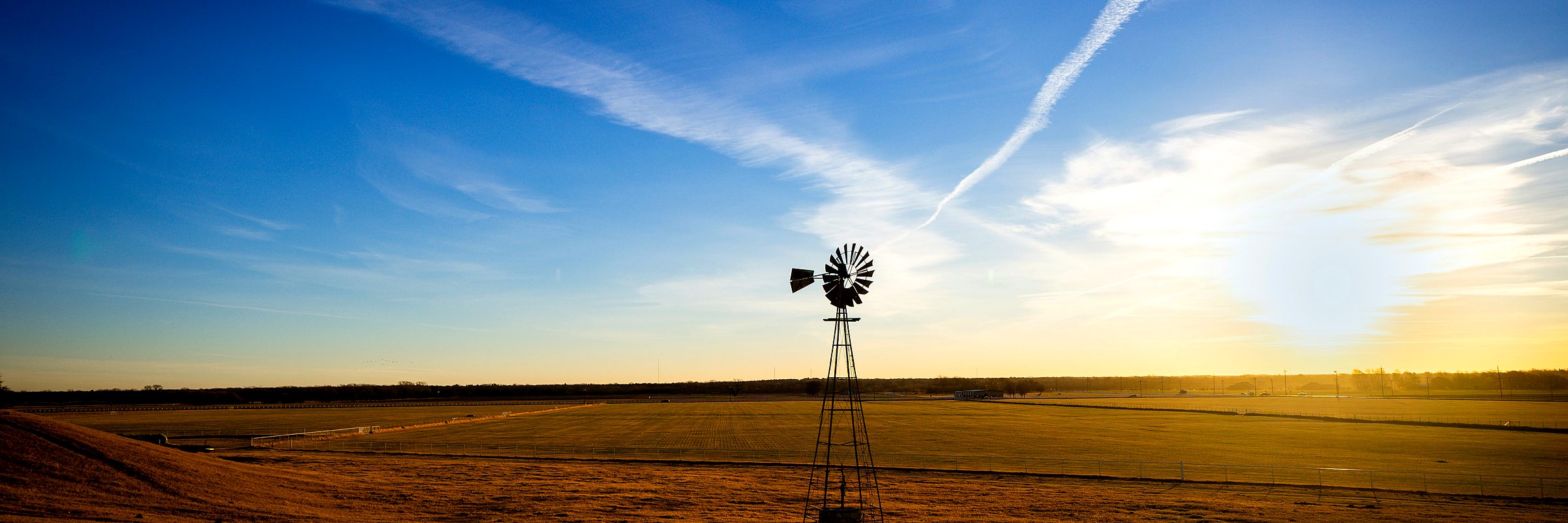 A windmill standing over open prairie at sunset